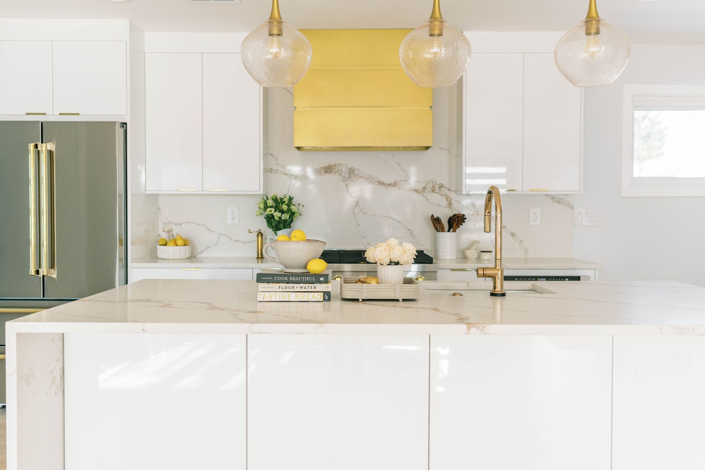 Modern white kitchen with a brass range hood, globe pendants and a waterfall island